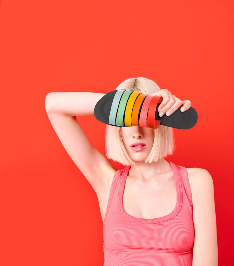 Model holding the handmade Sunshine women's slip-on leather sandals in black insole with rainbow straps / RAINBOW